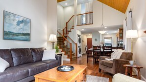 A spacious living room with a leather sofa, wooden coffee table, and a dining area with a table and chairs. A staircase leads to an upper level. - Right across from the pool & hot-tub! (Parksville)