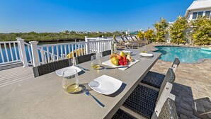 Ein Esstisch mit Obstplatte, Weingläsern und Besteck mit Blick auf einen Swimmingpool und eine schöne Aussicht.