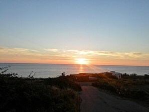 A coastal road leading to a beach with a sunset in the background.