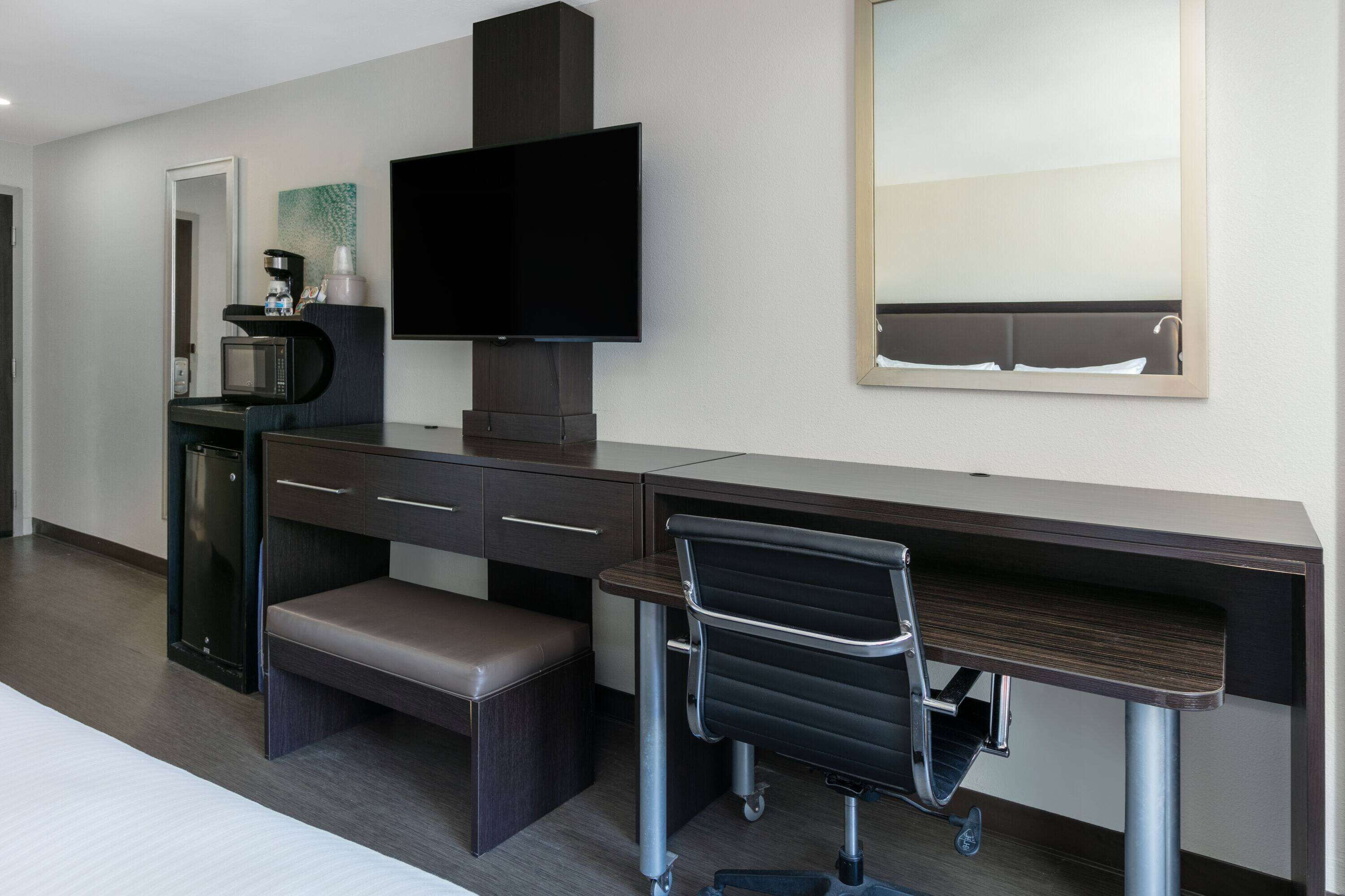 Een hotelkamer met een bureau, een stoel, een televisie, een magnetron en een koffieapparaat.