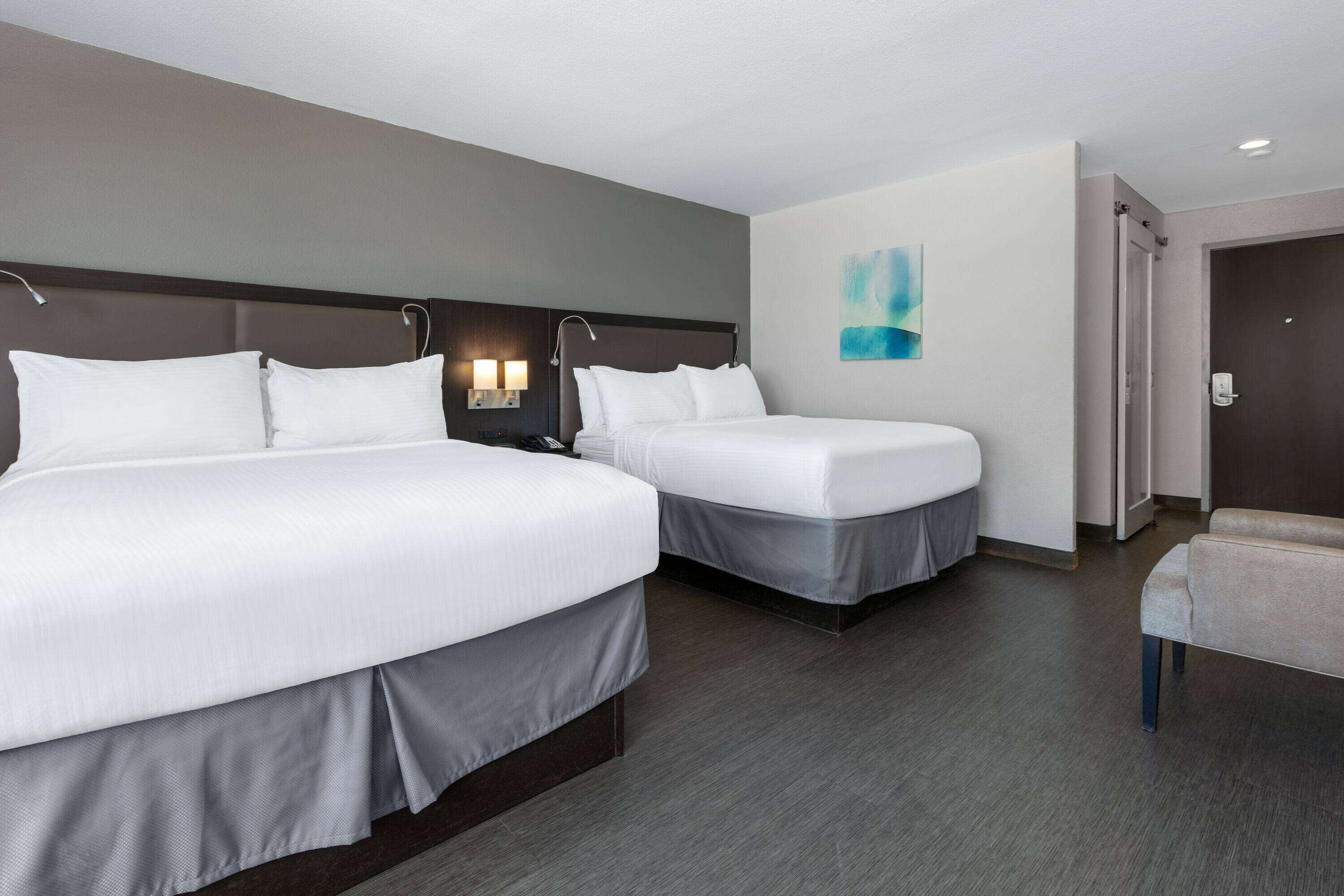 Une chambre d’hôtel avec deux lits, une table de chevet avec une lampe, un tableau au mur et une porte donnant sur une salle de bain.