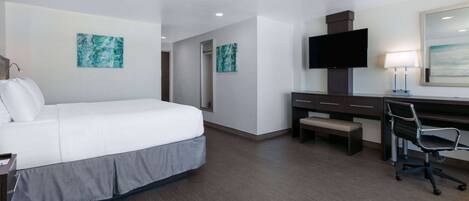 A hotel room with a large bed, a desk with a chair, a flat-screen TV, and artwork on the walls.
