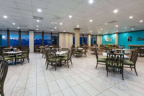 A spacious restaurant with high ceilings, large windows offering city views, and a blue accent wall.