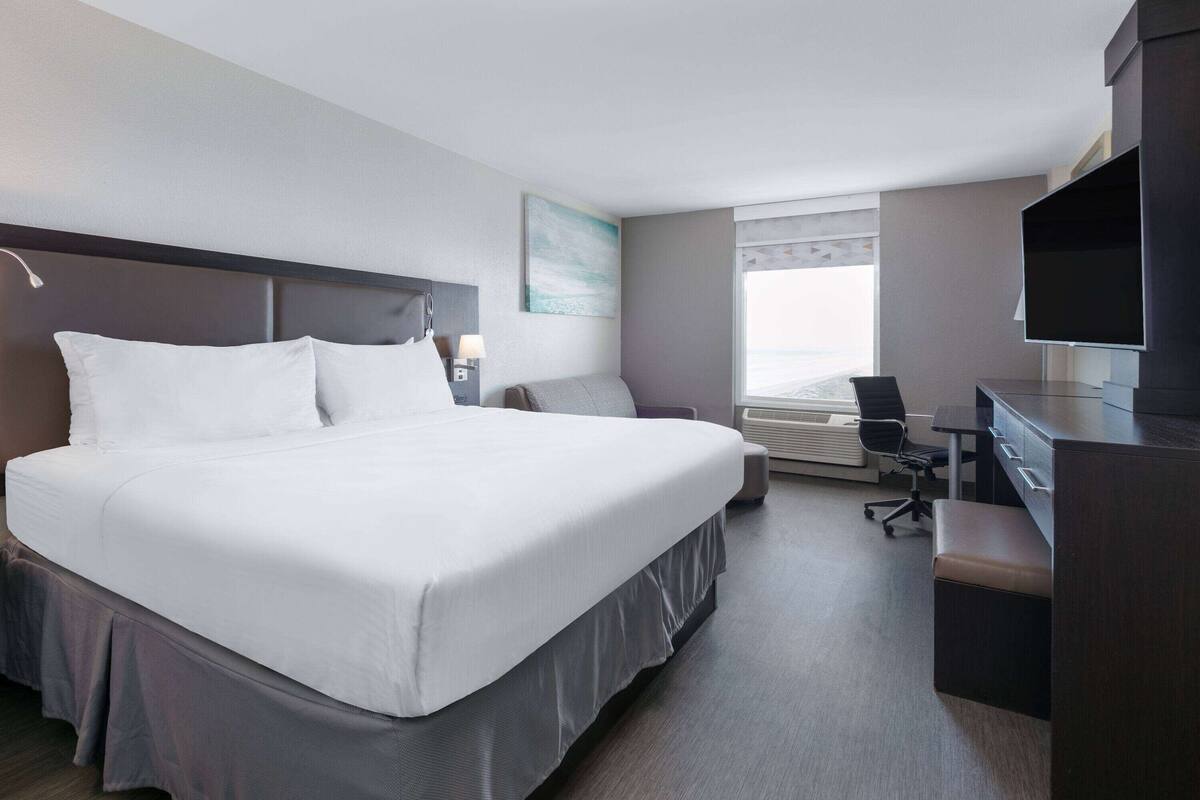 Een moderne hotelkamer met een groot bed, een bureau, een stoel, een televisie en een raam met jaloezieën.