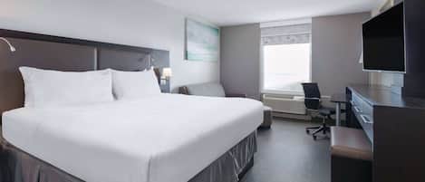 Quarto de hotel moderno com uma cama grande, uma escrivaninha, uma cadeira, uma televisão e uma janela com persianas.