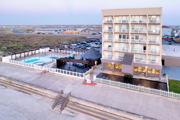 A hotel with multiple floors, a swimming pool, and a covered outdoor area with seating.