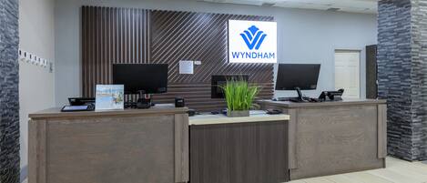 A reception desk with a logo, two monitors, a plant, and a sign.