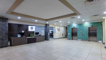 Zona de recepción con mostrador, una computadora y el logo de Wyndham. Se observan dos ascensores y una pared con diseño decorativo.