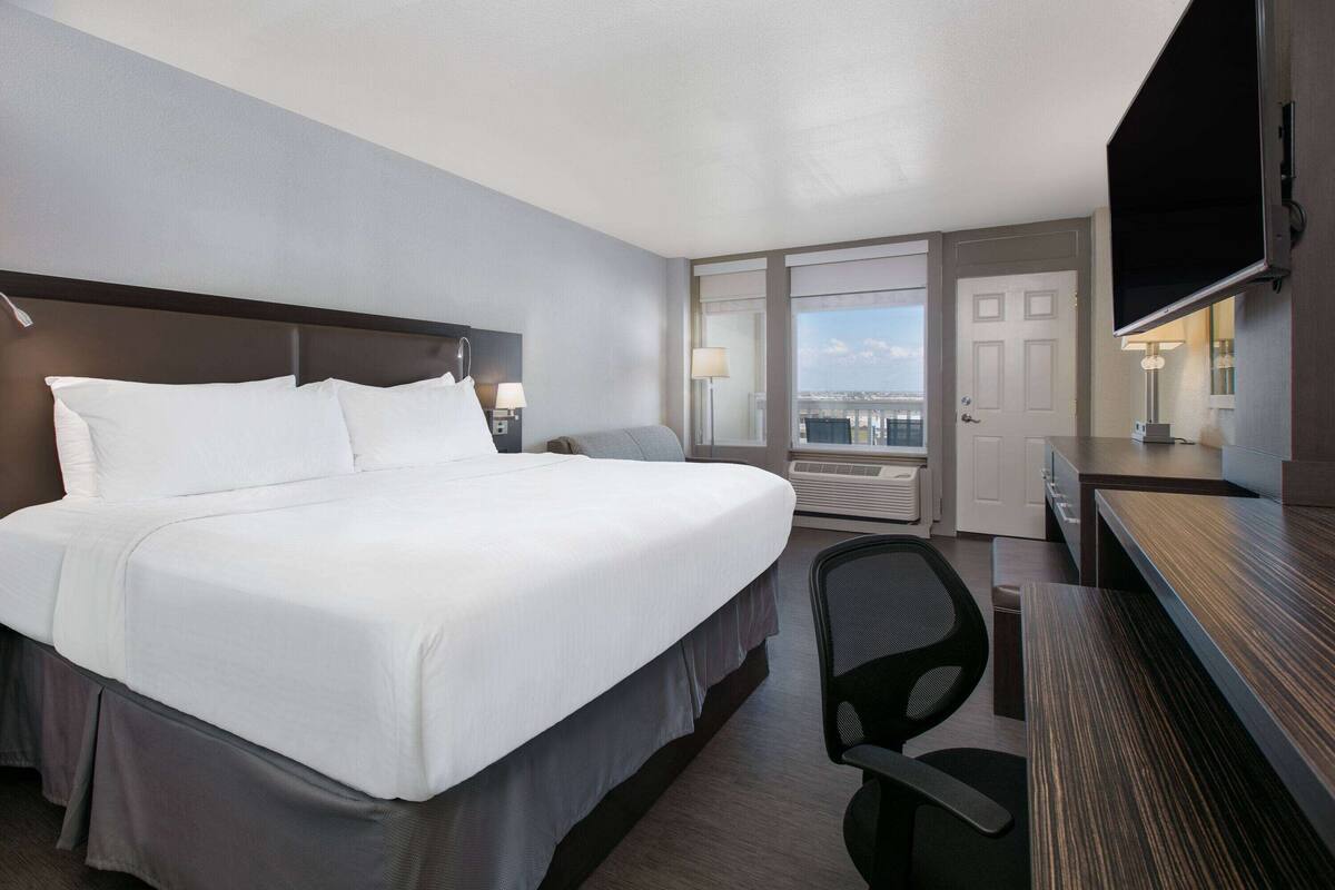 Een hotelkamer met een groot bed, een bureau, een stoel, een televisie en uitzicht op de stad.