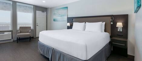 A hotel room with a large bed, a chair, a nightstand with a lamp, and a window with blinds.