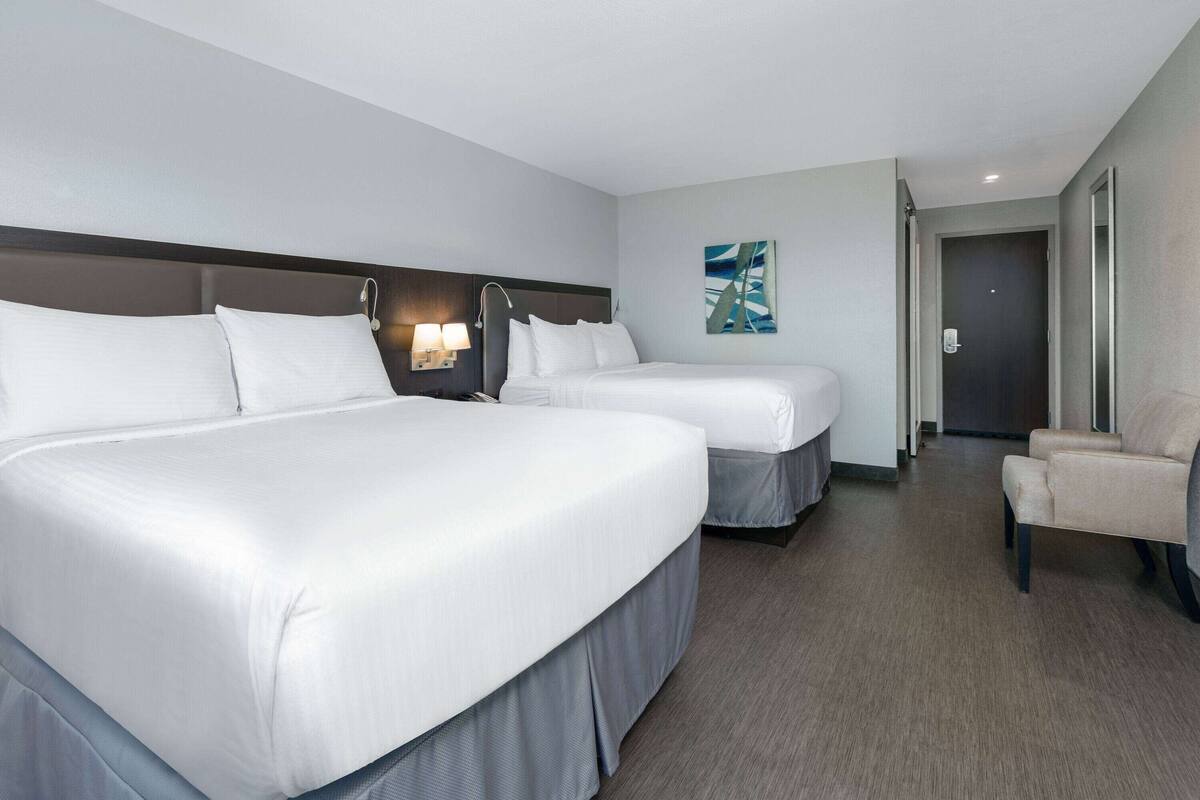 Een hotelkamer met twee bedden, een stoel en een schilderij aan de muur.