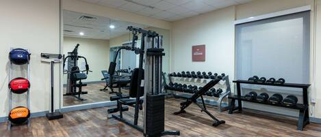 Une salle de sport équipée de matériel d’exercice, de supports pour les poids et d’un miroir.