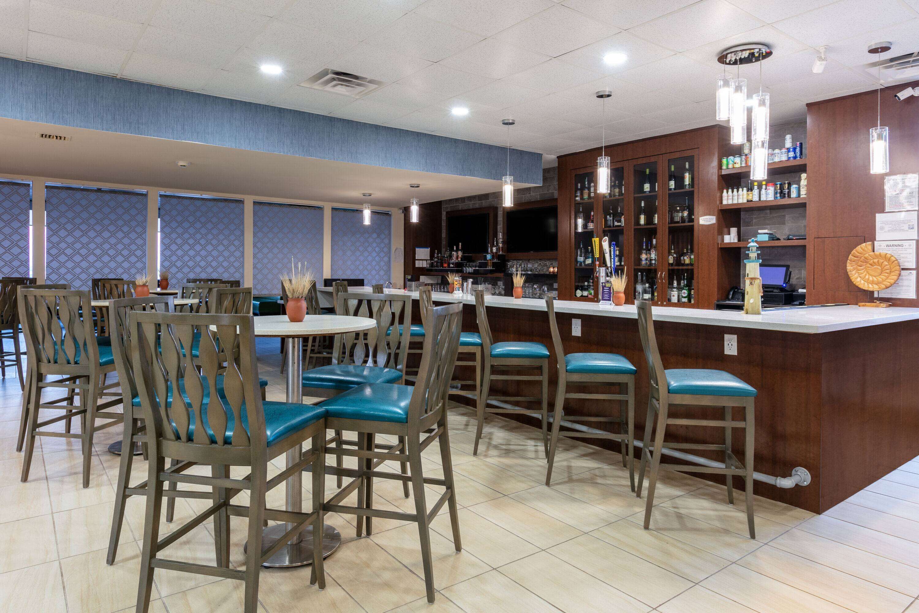 Un restaurante con zona de bar, sillas de madera con cojines azules y suelo de baldosas.