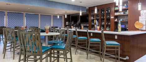 Un restaurante con zona de bar, sillas de madera con cojines azules y suelo de baldosas.