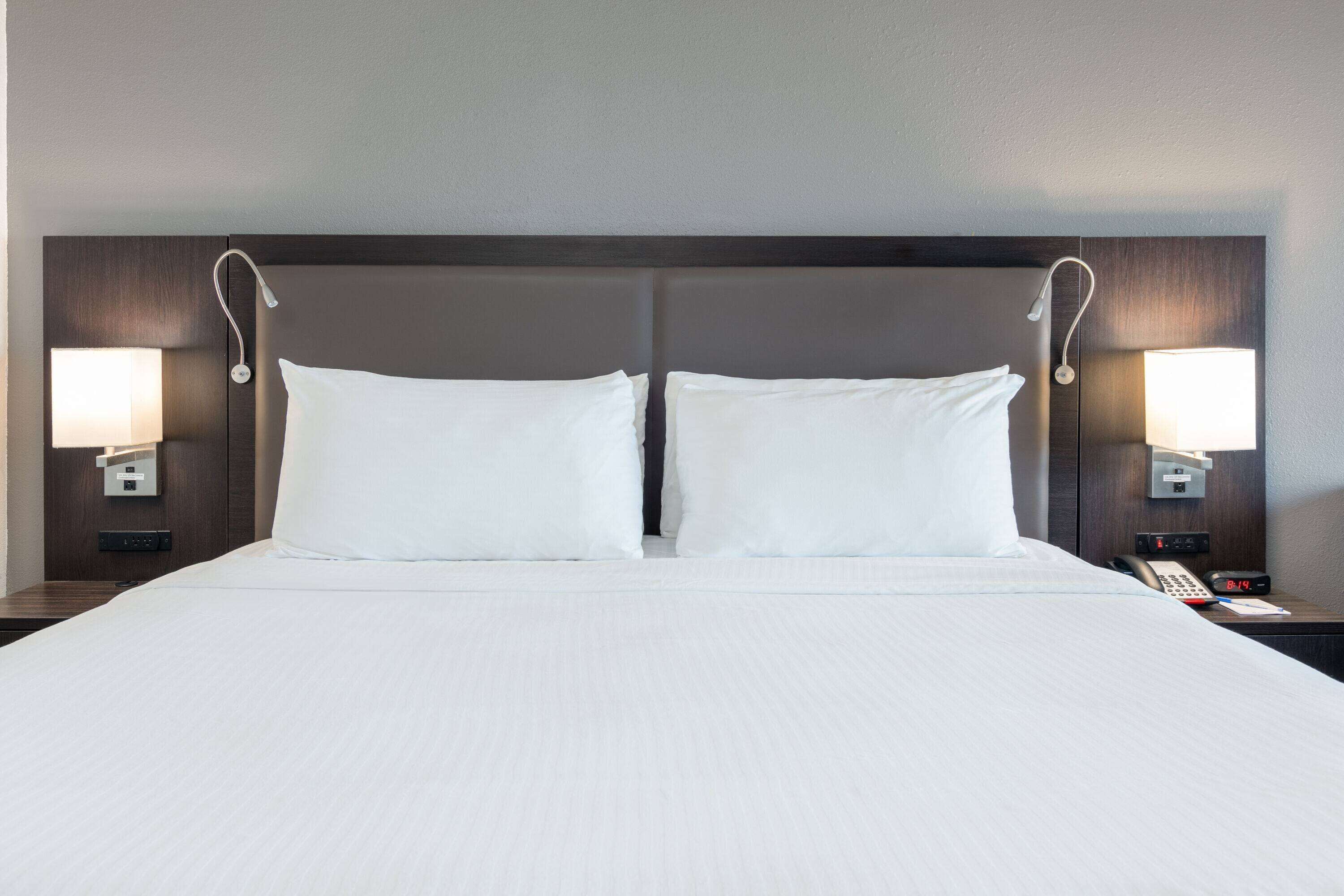 Une chambre d  ’hôtel dotée d’un grand lit, de deux lampes de chevet, d’une table de chevet avec un téléphone et une horloge, et d’une tête de lit avec un éclairage intégré.