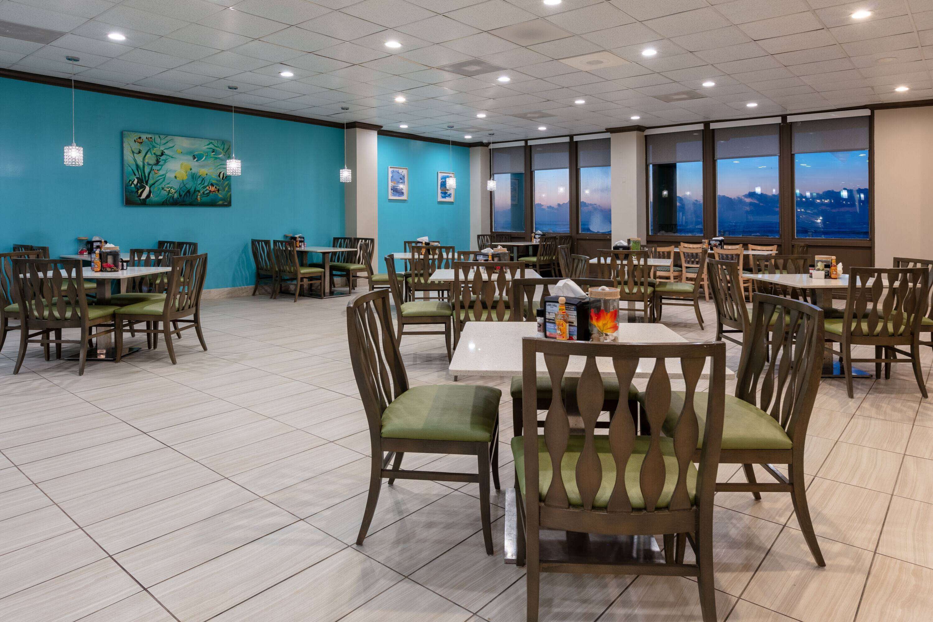 A spacious dining area with multiple tables and chairs, large windows with a city view, and a blue accent wall.