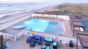 A rooftop pool area with a view of the beach, lounge chairs, and a small hot tub.