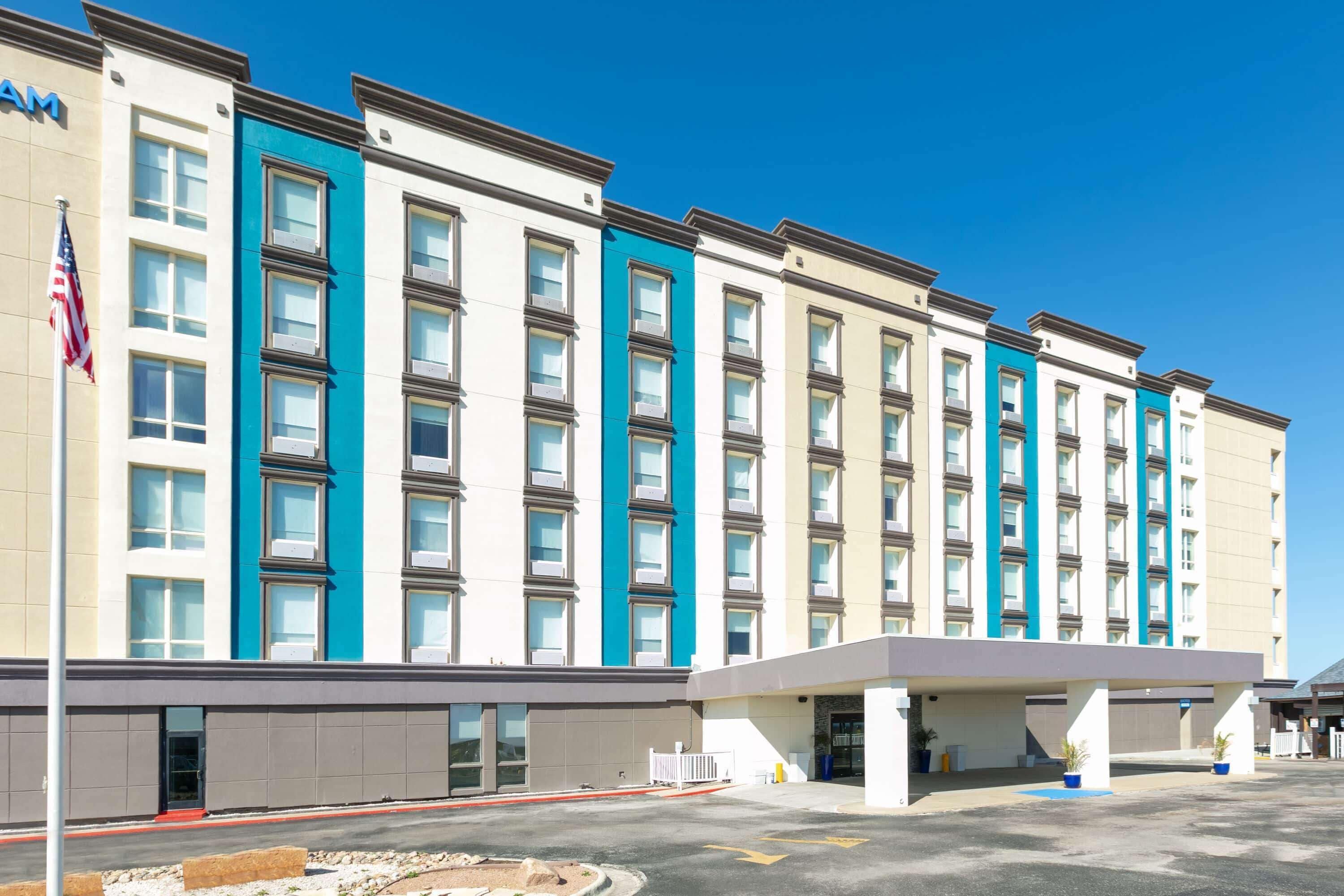 A multi-story hotel with a flat facade, large windows, and a parking lot in front.