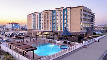 A hotel with a swimming pool, outdoor seating, and a view of the cityscape.