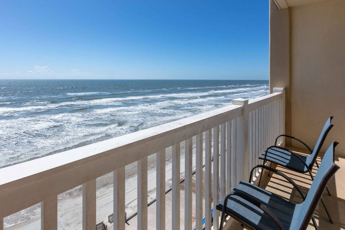 Een balkon met uitzicht op de oceaan, met twee stoelen en een hekwerk.