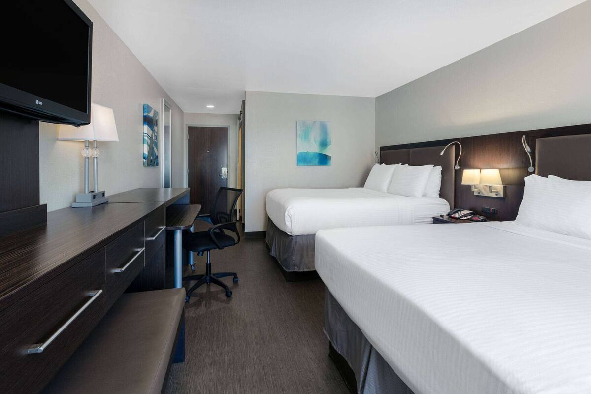 Een hotelkamer met twee bedden, een bureau, een televisie en kunst aan de muren.