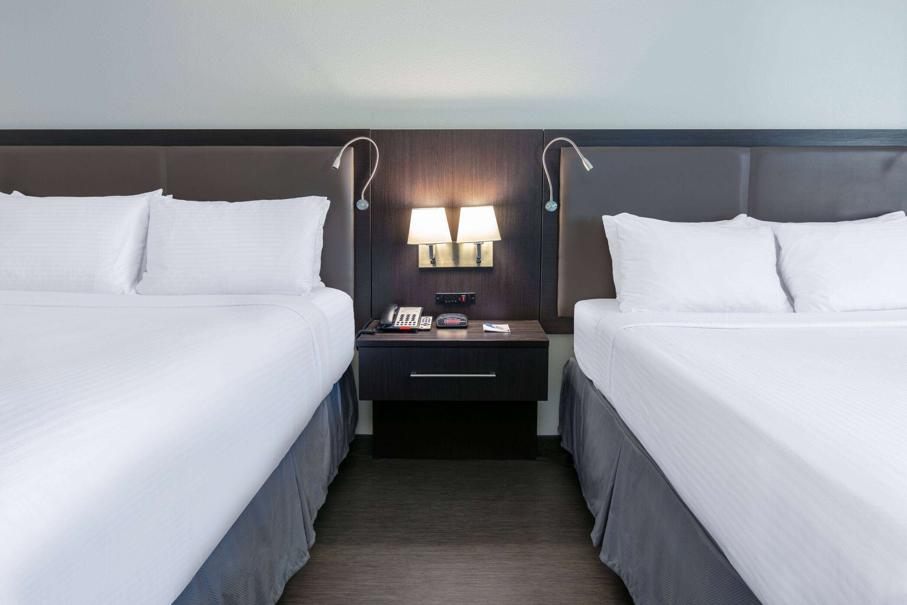 Habitación de hotel con dos camas, una mesita de noche con lámparas, un teléfono y un reloj digital.