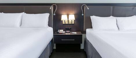 A hotel room with two beds, a nightstand with lamps, a phone, and a digital clock.