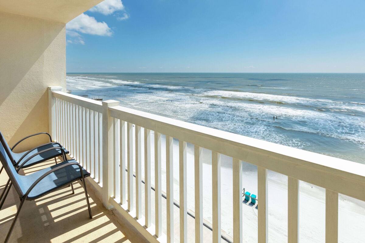 Een balkon met uitzicht op de oceaan, een witte reling en twee stoelen.