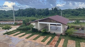 Um edifício moderno com área de estacionamento coberta, rodeado por jardins bem cuidados e um caminho pavimentado.