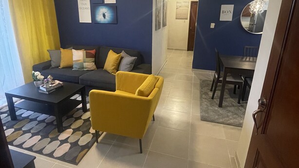 Uma sala de estar com sofá, poltrona amarela, mesa de centro e um espaço de jantar com mesa e cadeiras.