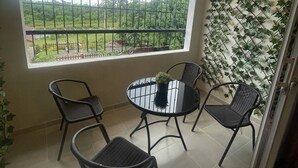 Uma varanda com vista para uma paisagem verde, uma mesa redonda com cadeiras e uma parede com trepadeira.