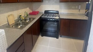 Cozinha compacta com armários de madeira escura, fogão preto e painel de azulejos.