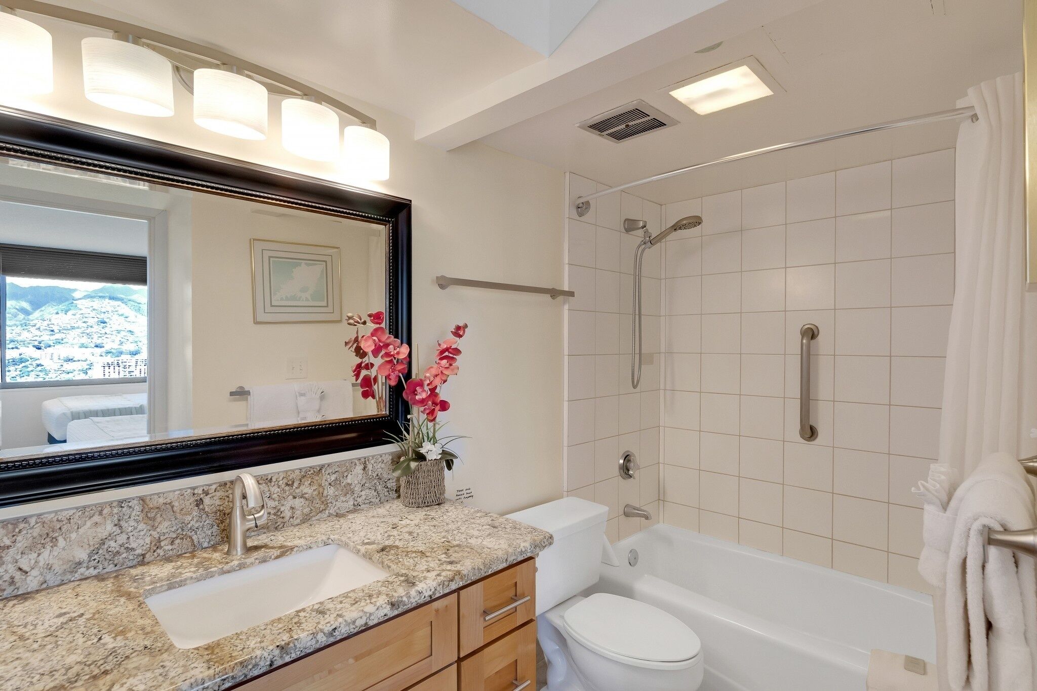 A bathroom with a granite countertop, white sink, and a large mirror. There is a shower area with a glass door and a towel rack.