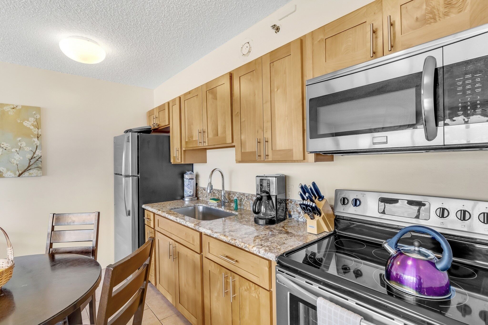 A kitchen with wooden cabinets, a stainless steel refrigerator, a microwave, a gas stove, and a sink.
