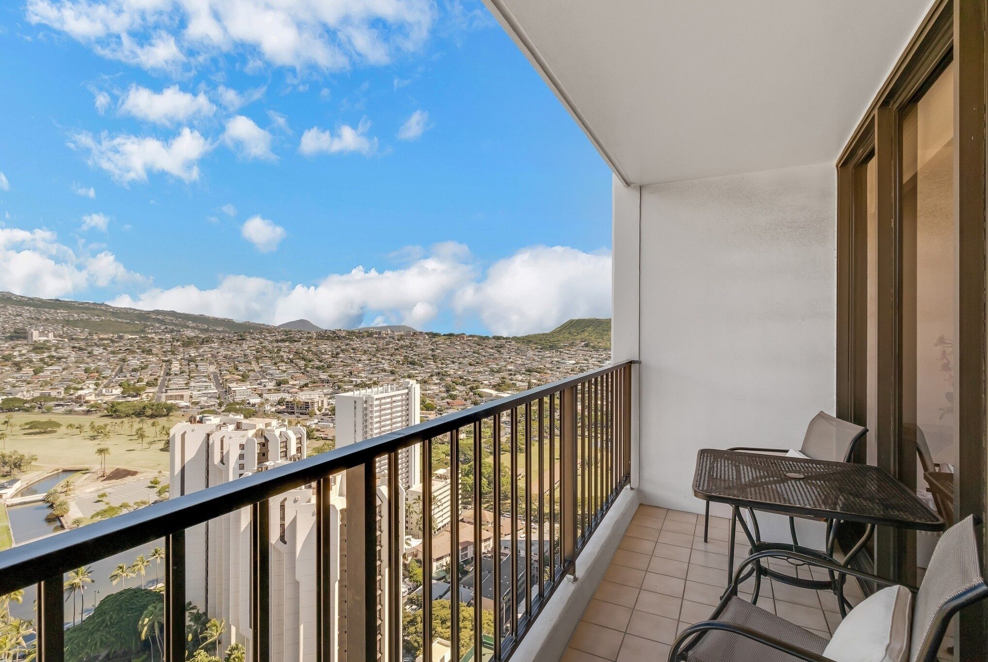 A balcony with a view of a cityscape, a table, and chairs.