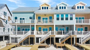 A multi-story beachfront building with balconies, wooden decks, and a sandy ground. - Pelican's Perch (Port St. Joe)