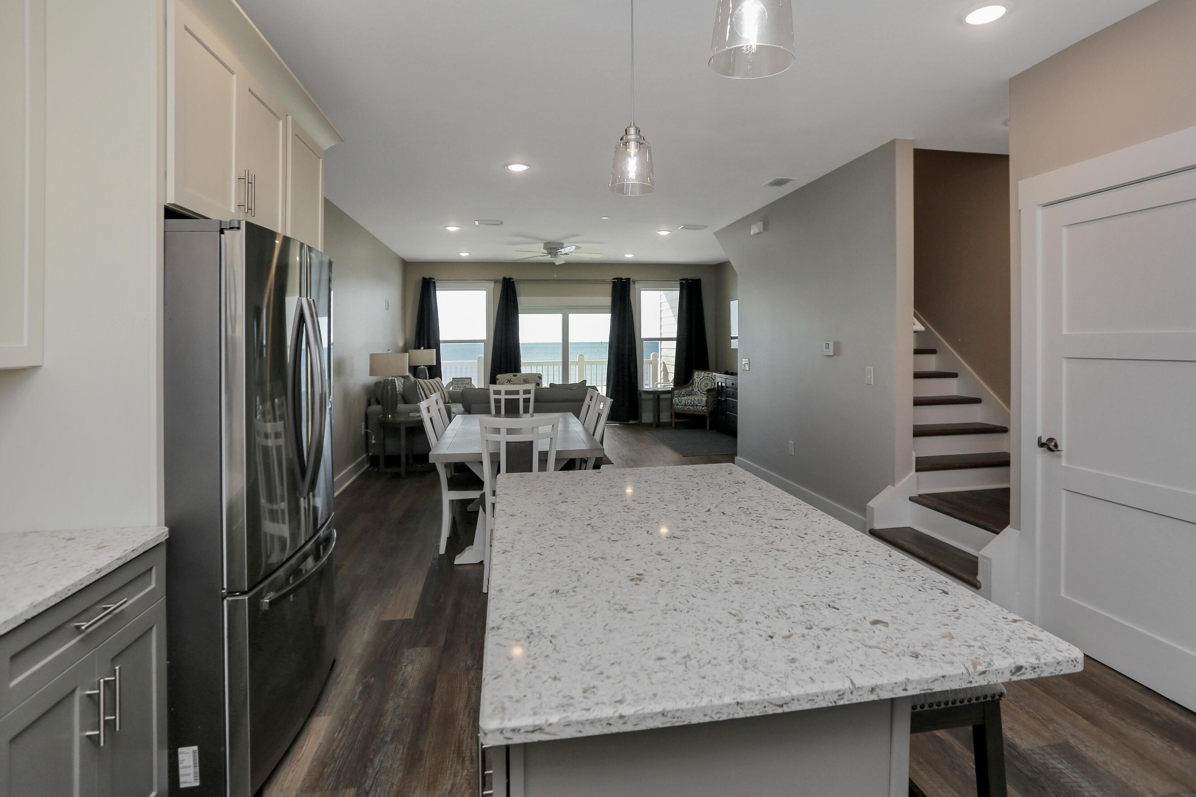 A modern kitchen with a large island, stainless steel appliances, and a dining area with a view of the ocean.
