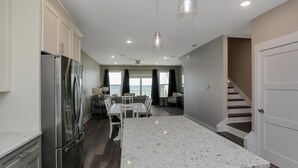 A modern kitchen with a large island, stainless steel appliances, and a dining area with a view of the ocean. - Pelican's Perch (Port St. Joe)