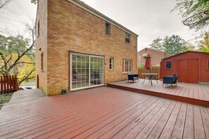 Une maison en briques dotée d’une grande porte-fenêtre coulissante, d’une terrasse en bois et d’un petit espace patio aménagé avec du mobilier d’extérieur.