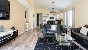 Un salon moderne avec un canapé en cuir noir, une table basse en verre et un tapis à motifs noir et blanc.