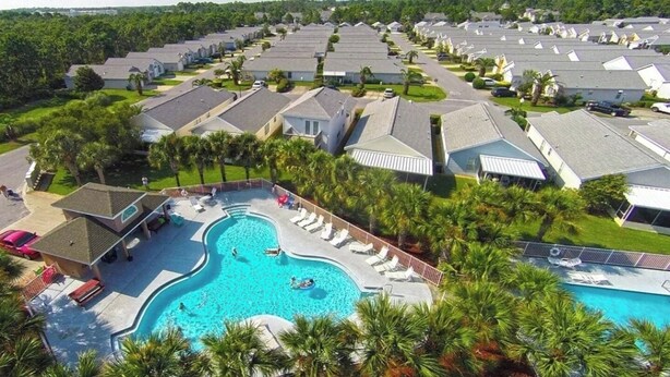 Un quartier résidentiel doté d’une piscine entourée de chaises longues et de palmiers.