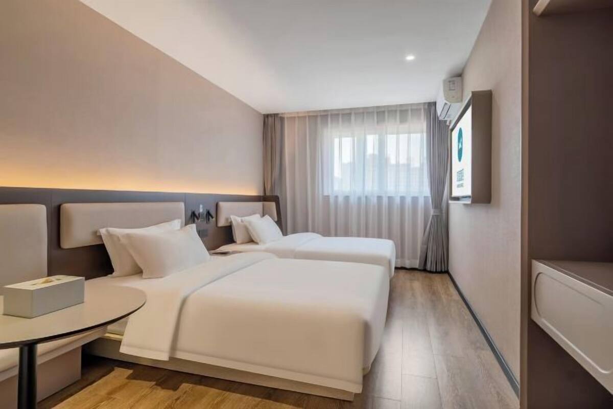 A hotel room with a bed, bedside table, and a window with curtains.