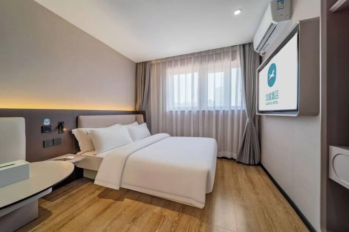 A hotel room with a bed, bedside table, and a TV mounted on the wall.