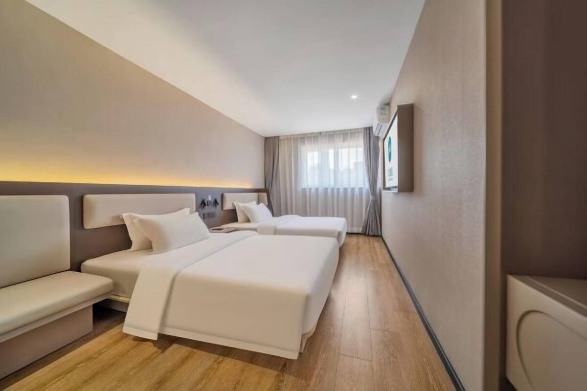 A hotel room with two beds, a sofa, a bedside table, and a window with curtains.