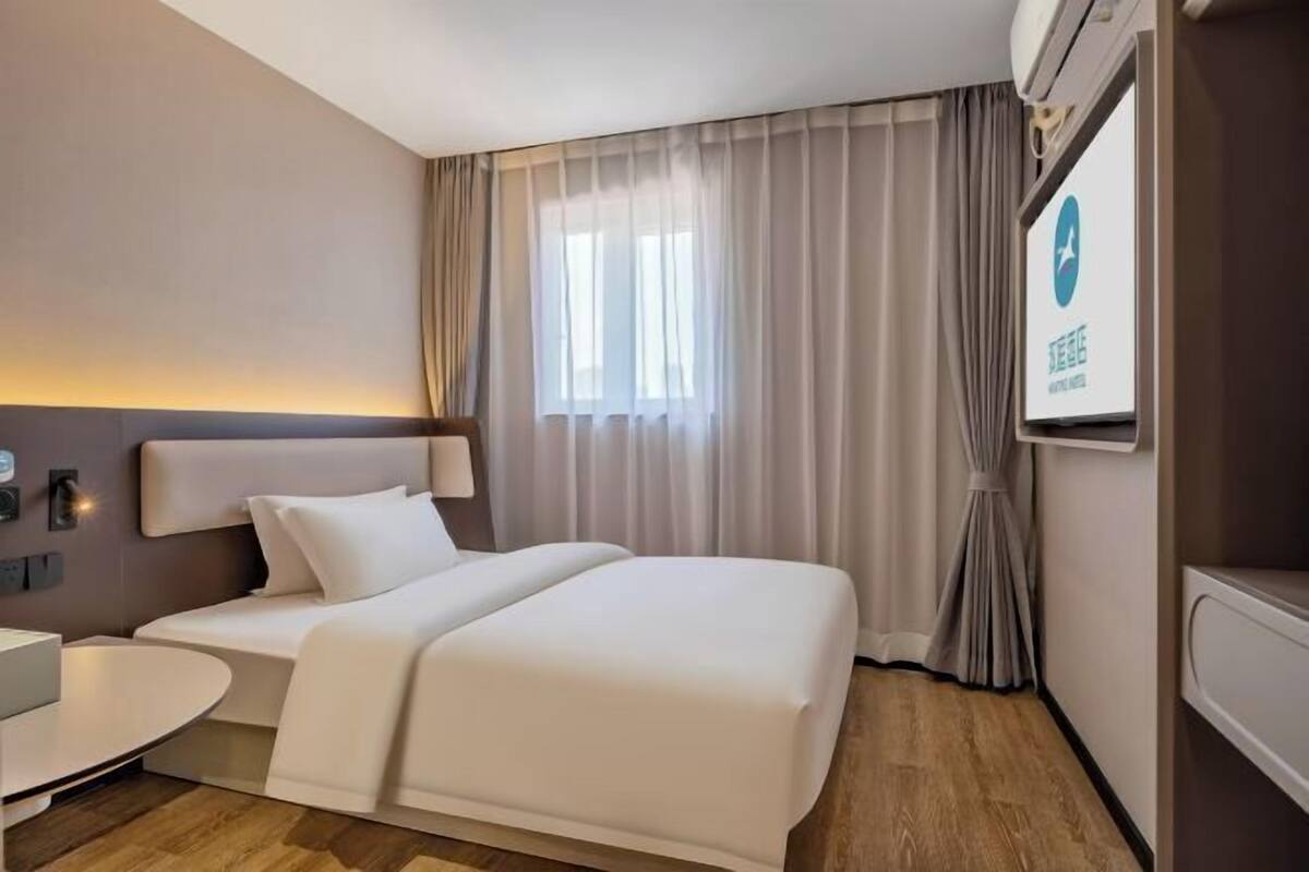 A hotel room with a bed, a desk, a chair, a TV, and a window with curtains.