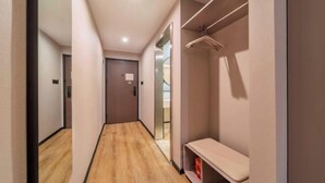 Un couloir avec un plancher en bois, un banc, un porte-manteau et une porte au fond.