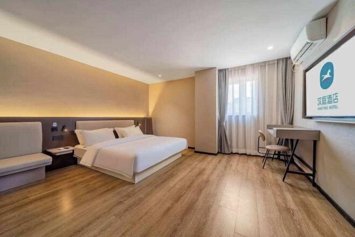A hotel room with a bed, a desk, a chair, a nightstand, and a large window with curtains.