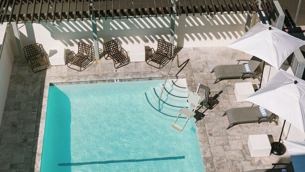 Vista aérea de una piscina con sillas de descanso y sombrillas, rodeada de baldosas de piedra.