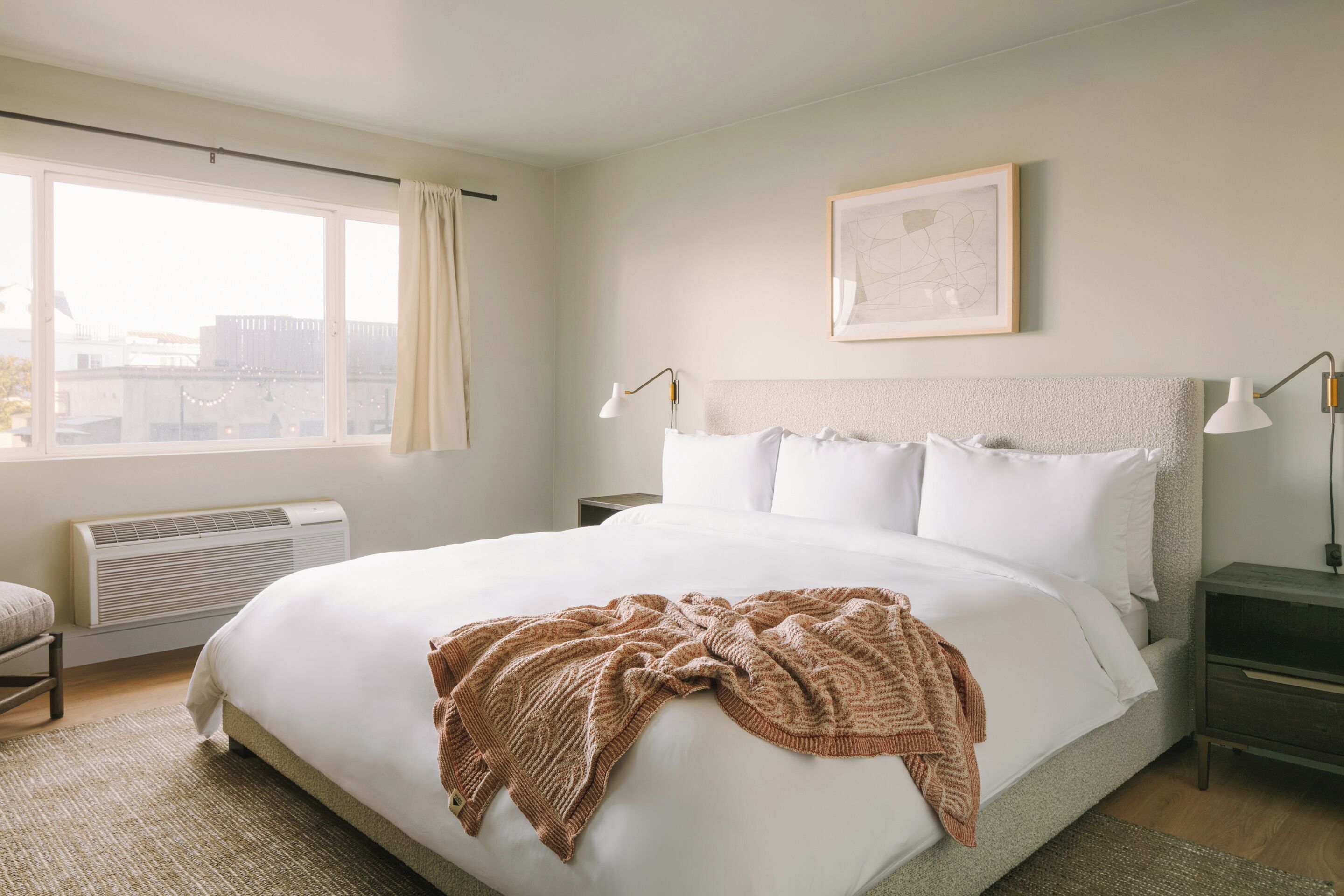 A neatly made bed with a patterned throw blanket, a bedside table with a lamp, and a framed picture on the wall.