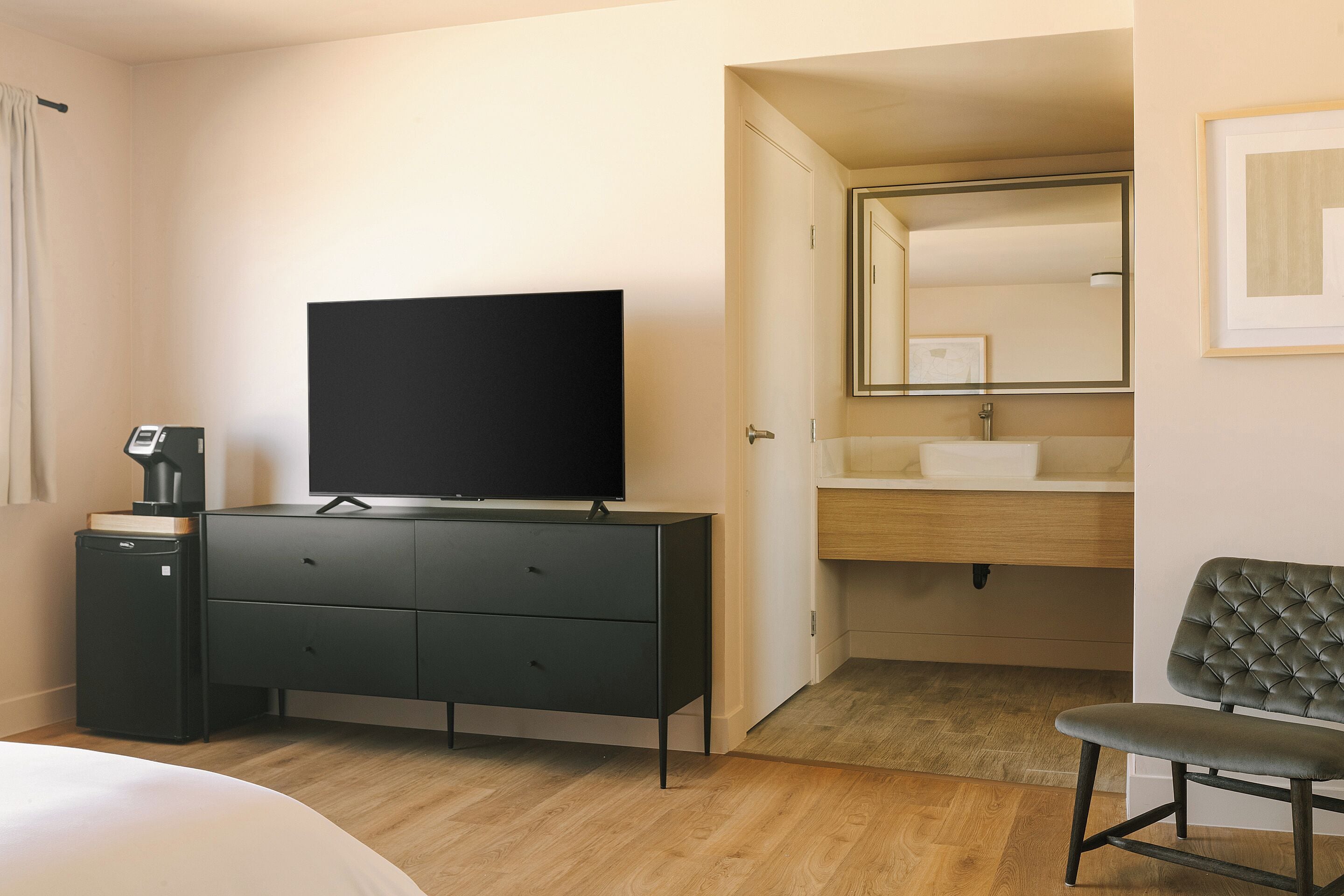 Hotelkamer met een bed, een televisie op een dressoir, een badkamer met spiegel en wastafel, en een stoel.